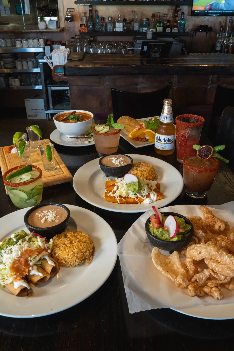 A full table spread of tacos, chicharrones, rice, salsas and a cold beer