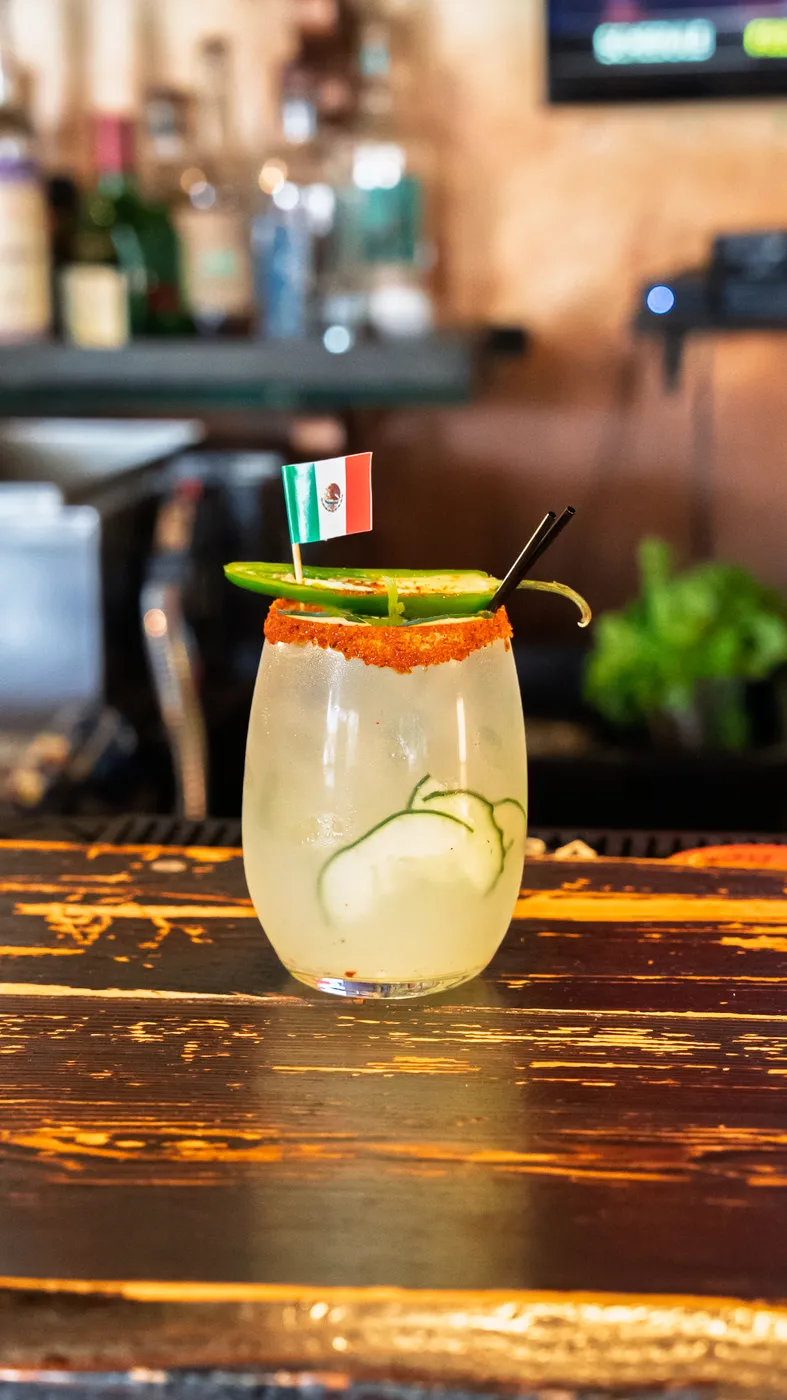 A cucumber margarita with a chile-salted rim on the bar